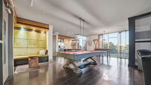 A modern indoor pool table with a wooden frame, a seating area with a patterned backrest, and a large window providing natural light.