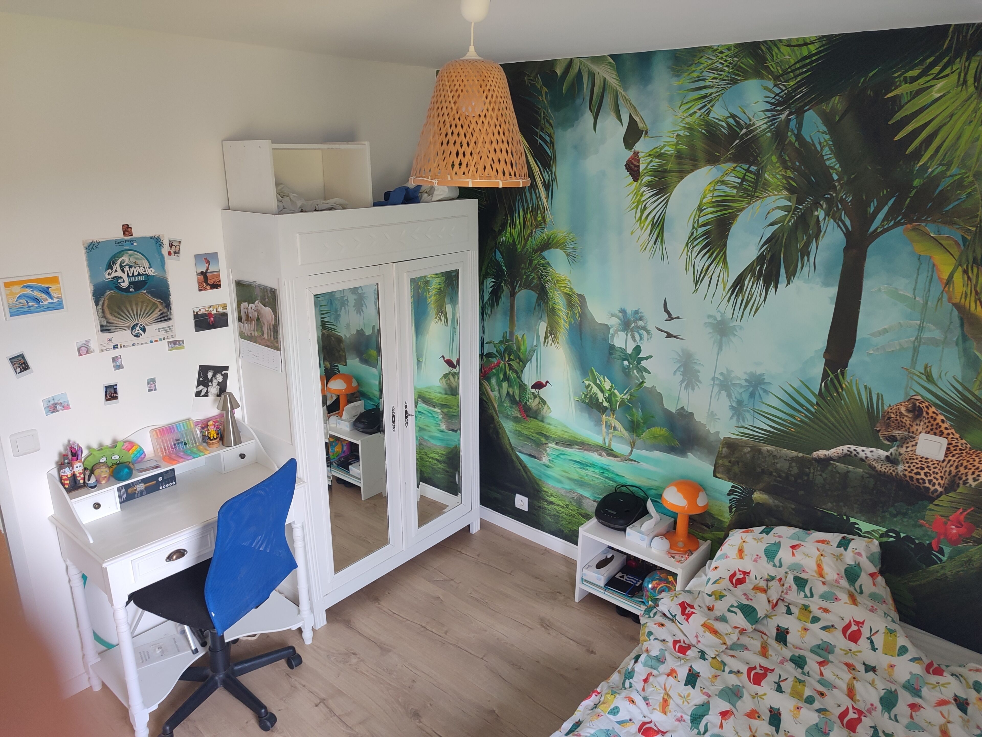 A bedroom with a desk, chair, bed, and a mural of a jungle scene.