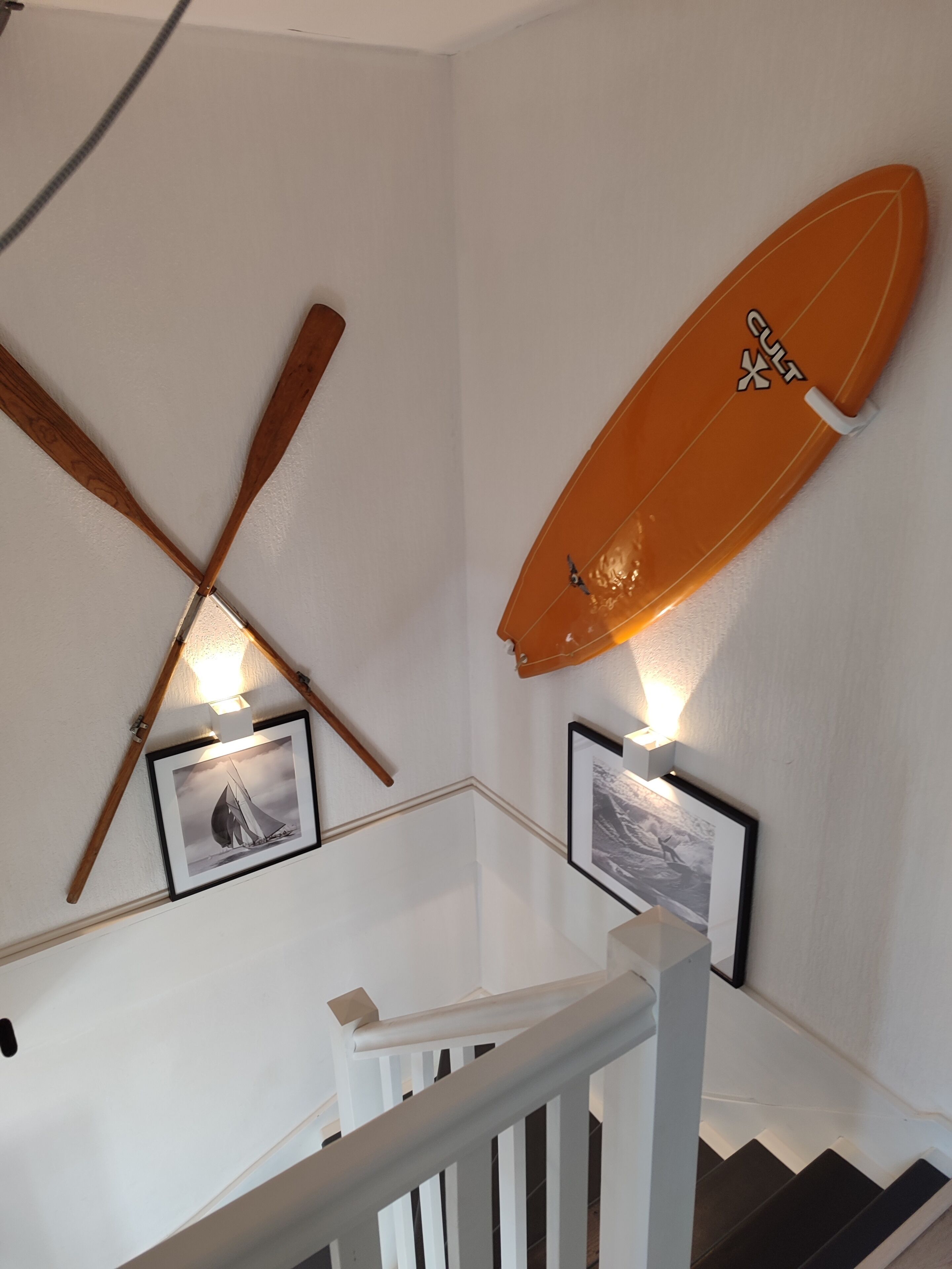 A staircase with a white railing, wooden handrails, and two framed photographs.