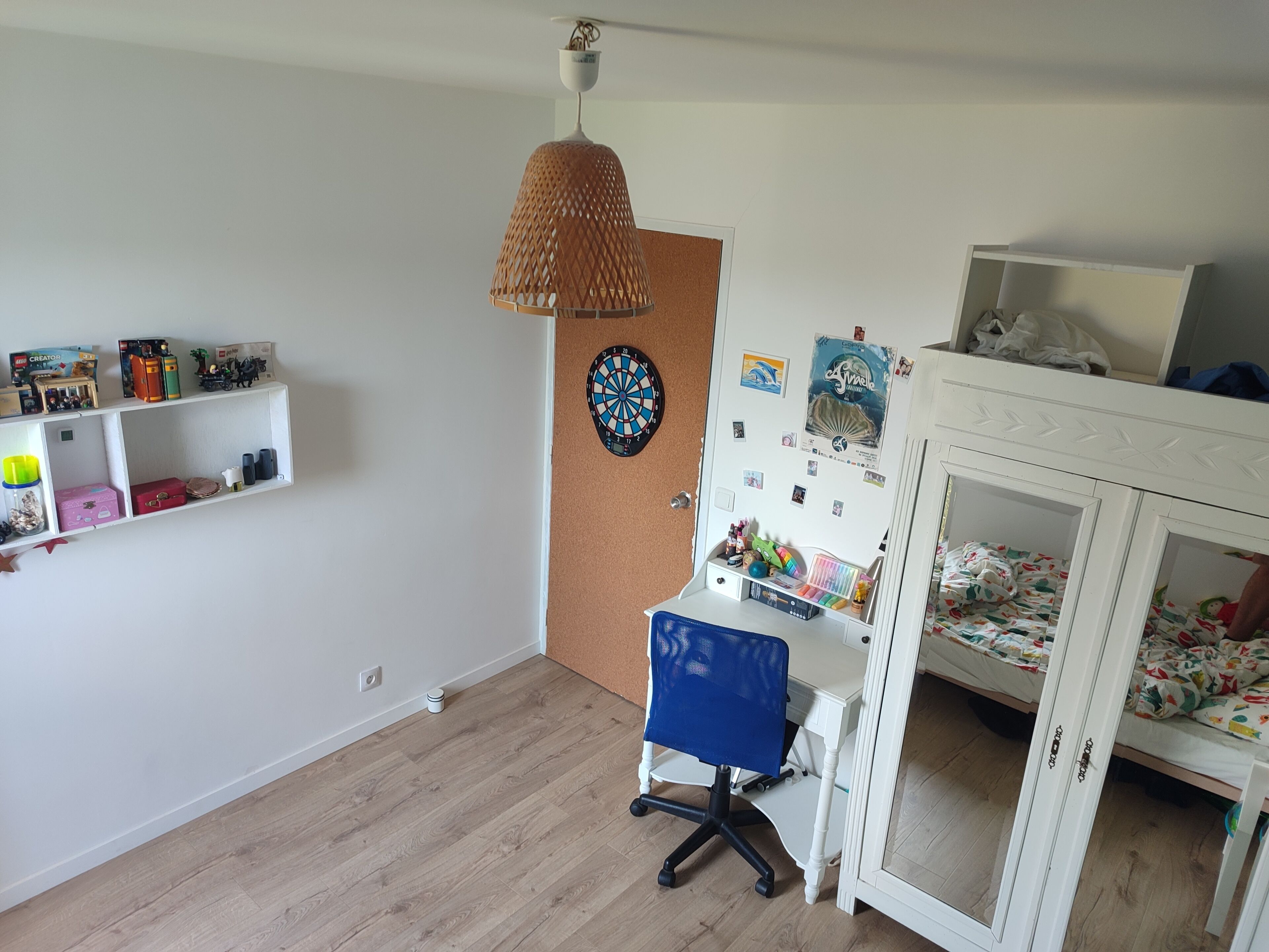 A room with a wooden floor, a desk with a chair, a bunk bed, and shelves with various items.