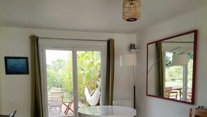 A room with a round table, a sofa, a hammock, a lamp, and a sliding glass door leading to an outdoor area with a table and chairs. - Cosy and quiet house between Landes and Pays Basque (Tarnos)