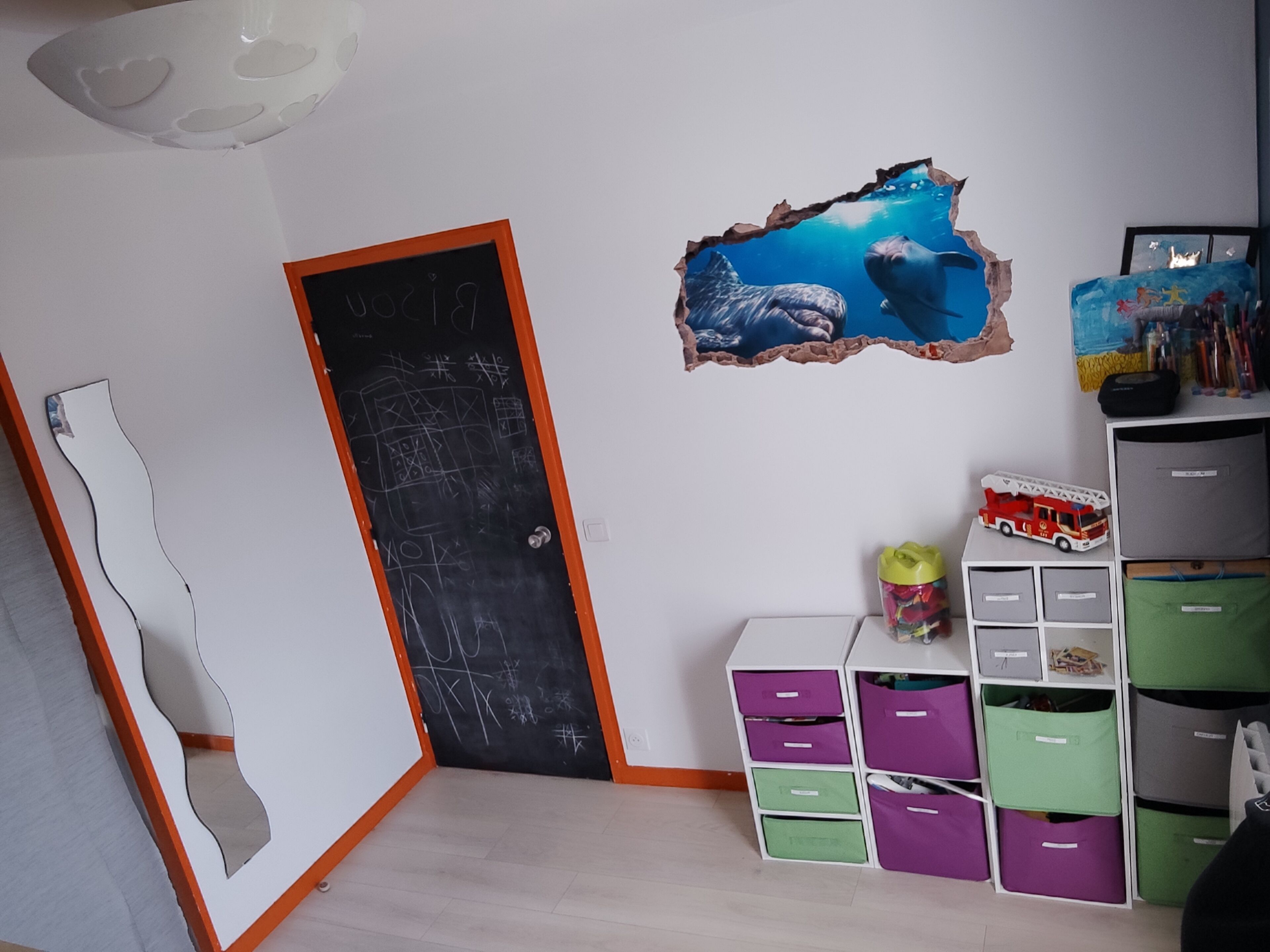 Una habitación con puerta de pizarra, pared con efecto de papel rasgado y unidades de almacenamiento con cajones.