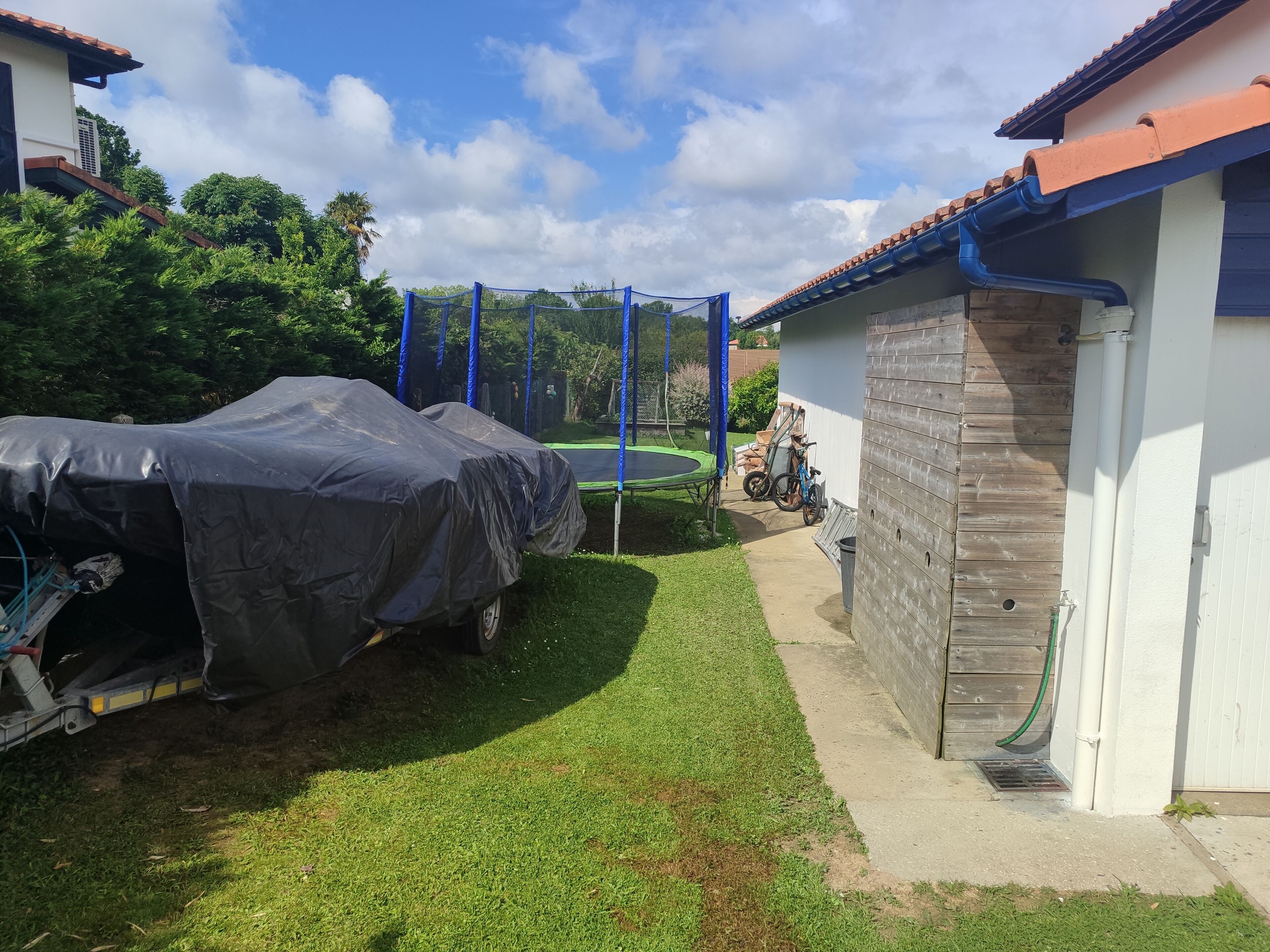 Ein überdachtes Fahrzeug, ein Trampolin und ein hölzernes Gartenhaus im Hinterhof.