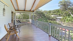 A covered porch with wooden flooring, a white railing, and a view of a hilly landscape.
