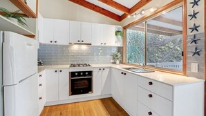 A modern kitchen with white cabinets, a built-in oven, and a large window with a view of trees.