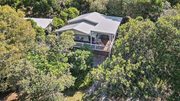 A house surrounded by dense greenery, with a covered porch and a visible deck area.