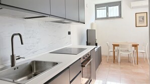Moderni keittiö, jossa on sisäänrakennettu liesi, pesuallas ja harmaat kaapit. Keittiössä on myös ruokailutila, jossa on pöytä ja tuolit.