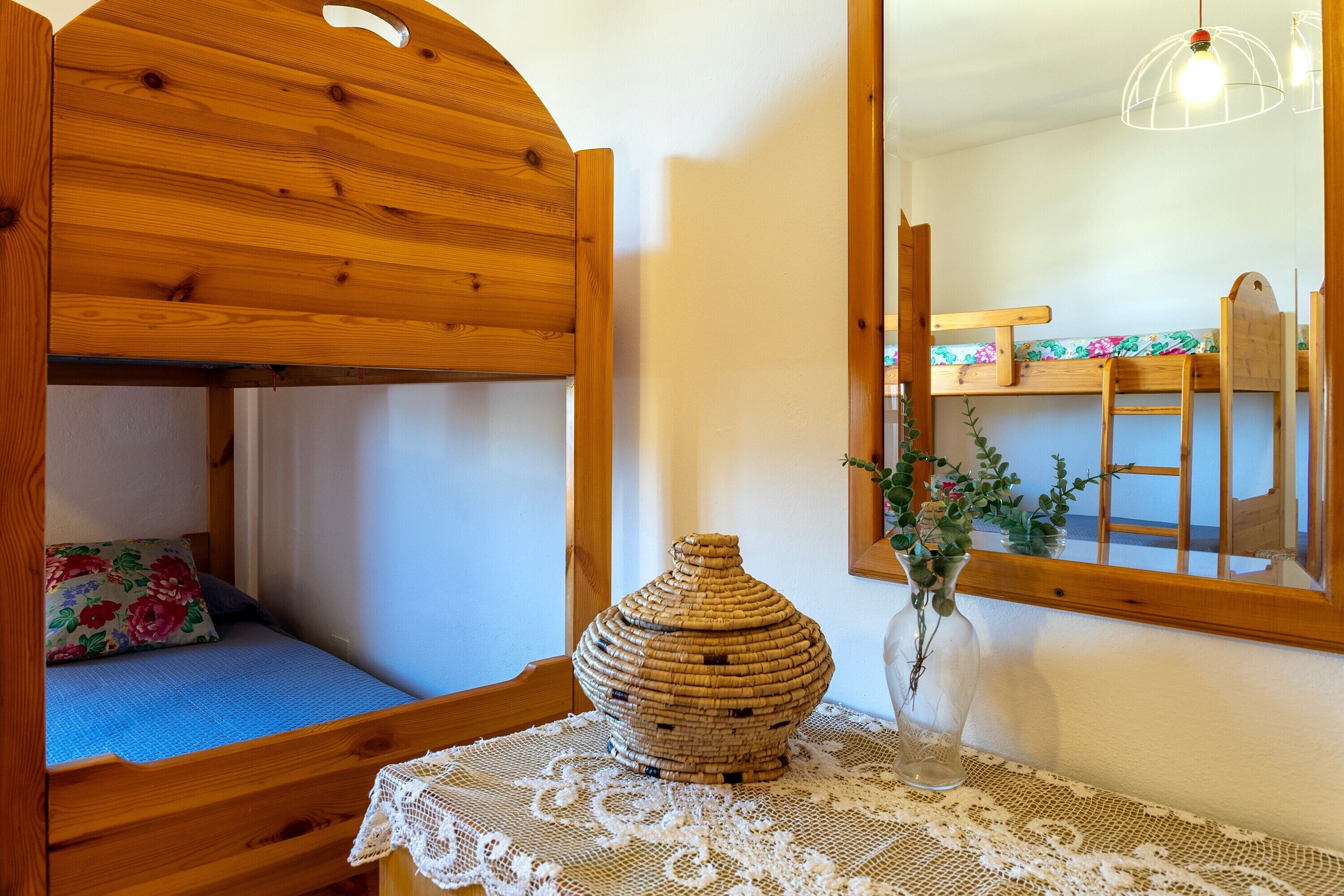 Un letto a castello in legno con un cuscino floreale, un vaso di vimini e una tovaglia di merletto.