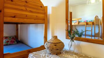 Un letto a castello in legno con un cuscino floreale, un vaso di vimini e una tovaglia di merletto.