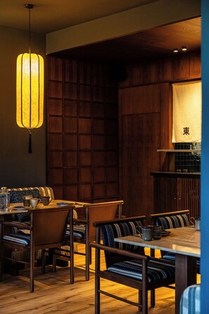 A restaurant interior with wooden paneling, a hanging light fixture, and a table set for dining. - chic&basic Tokyo Hoose (Porto)
