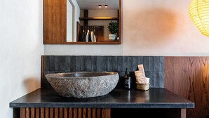 A bathroom with a large stone basin, a wooden vanity, a mirror, and a wall-mounted light fixture. - chic&basic Tokyo Hoose (Porto)