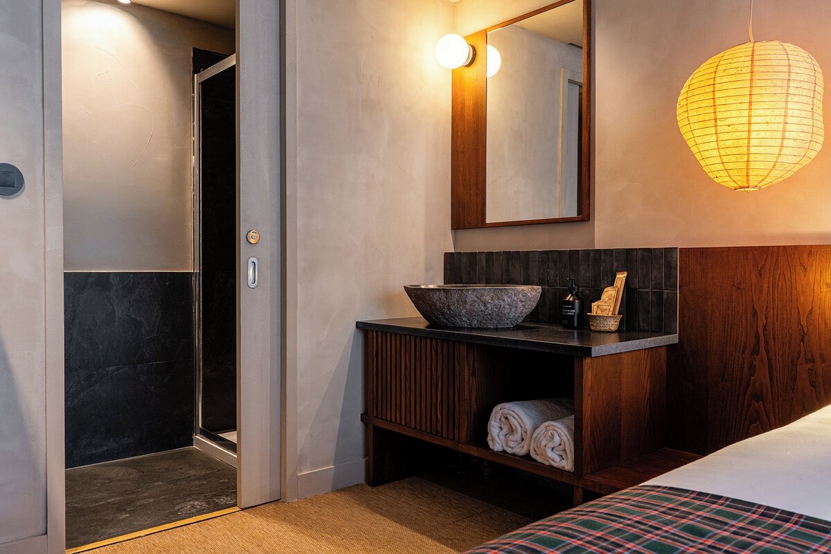 Une salle de bain d’hôtel avec un grand miroir, un meuble-lavabo en bois, un lavabo en pierre et un porte-serviettes.