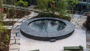 A circular hot tub surrounded by lounge chairs, a stone pathway, and a building with a green roof. - chic&basic Tokyo Hoose (Porto)