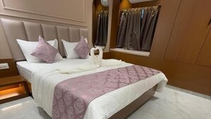 A modern hotel room with a large bed, a built-in vanity, and a window with curtains. - Hotel Shloka (Navi Mumbai)