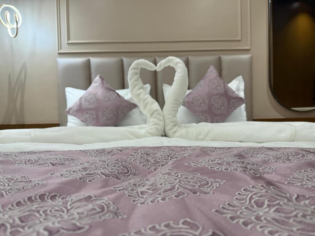 A bed with a heart-shaped pillow arrangement, a patterned bedspread, and a headboard with a mirror.