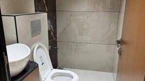 A bathroom with a toilet, a sink, and a marble wall. - Hotel Shloka (Navi Mumbai)