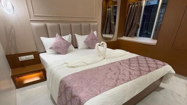 A modern bedroom with a large bed, a nightstand, a mirror, and an air conditioning unit. - Hotel Shloka (Navi Mumbai)