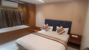 A hotel room with a bed, a window with curtains, a bedside table, and a wall-mounted air conditioner. - Hotel Shloka (Navi Mumbai)