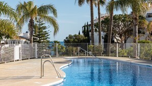 Una piscina con una scala in metallo, circondata da una recinzione bianca e palme.