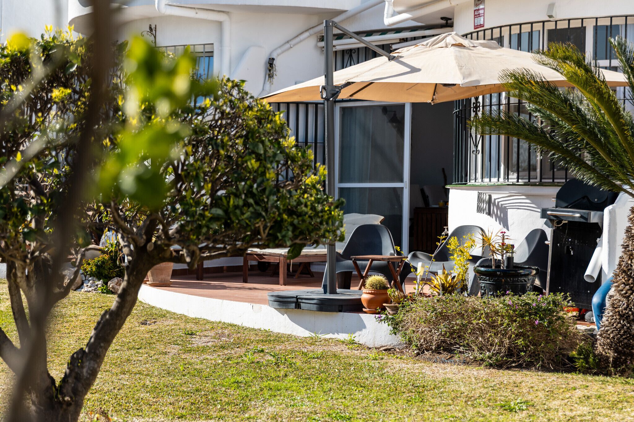 Un patio con mobiliario exterior, un parasol grande y plantas en macetas.