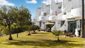 Un edificio bianco con un giardino antistante, che include una palma e un piccolo arbusto.