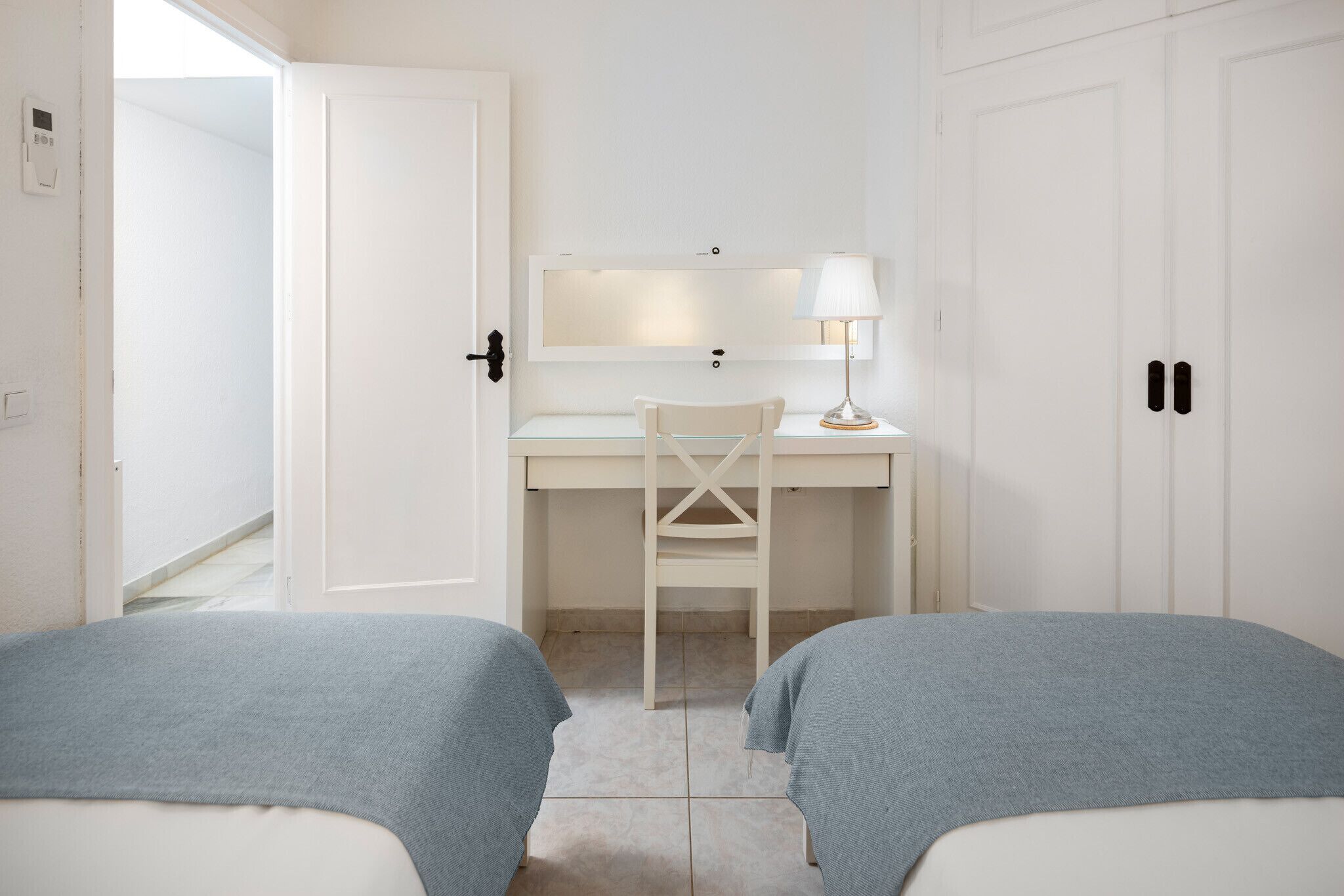 A bedroom with two beds, a desk, a chair, a lamp, and a wardrobe.