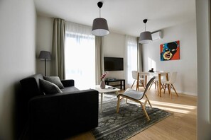 A modern living room with a black sofa, a coffee table, a TV, a dining area with chairs, and a painting on the wall. - Connect Living Serviced Apartments (Sofia)