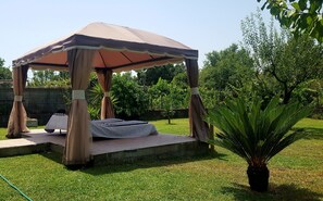 A gazebo with a canopy, a table, and chairs, surrounded by grass and trees.
