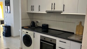 A modern kitchen with white cabinets, a washing machine, an oven, and a countertop with a toaster. - Comfortable apartment with balcony and huge pool (Sucina)