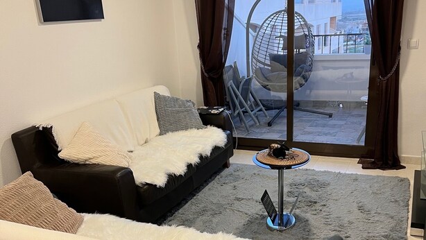 A modern living room with a sofa, a coffee table, and a view of a balcony with outdoor furniture. - Comfortable apartment with balcony and huge pool (Sucina)
