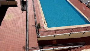 A rectangular swimming pool with a tiled deck, surrounded by a metal fence and a few potted plants. - Comfortable apartment with balcony and huge pool (Sucina)