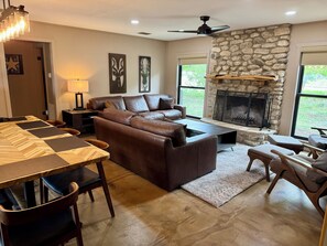 A living room with a stone fireplace, leather sofa, dining table, and a ceiling fan.