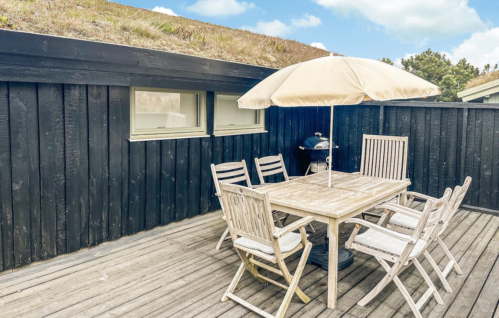 En træterrasse med et bord, stole, grill og stor parasol.