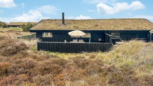 Une maison moderne avec un toit plat, une cheminée et une petite terrasse dotée de meubles pour se détendre en plein air.