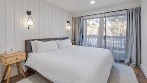 Une chambre dotée d’un grand lit, de deux appliques murales, d’une table de chevet en bois et offrant une vue sur l’extérieur grâce à une fenêtre agrémentée de rideaux.