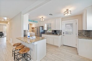 A modern kitchen with white cabinets, granite countertops, and a built-in island with bar stools. - Perfect oasis with private pool and wrap around deck! (Port Aransas)