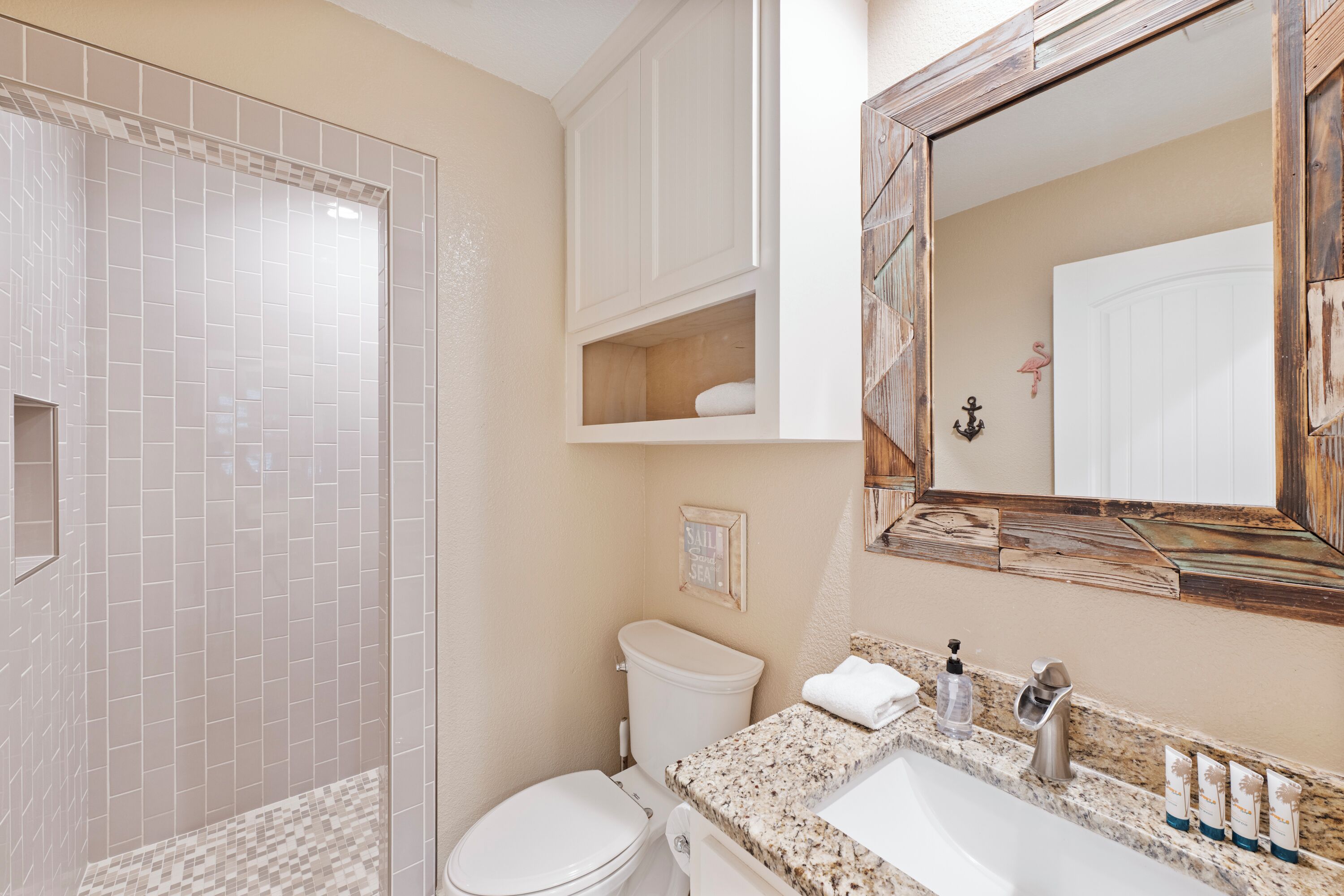 A bathroom with a shower, toilet, vanity, and a large mirror.