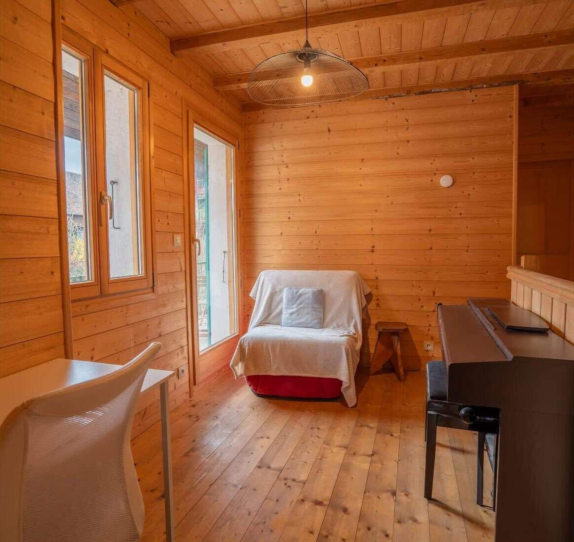 A wooden cabin interior with a bed, a table, and a chair.