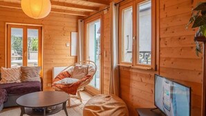 A cozy wooden cabin interior with a sofa, a chair, a bean bag, a TV, and large windows. - Maison méserier I T3 I Publier (Publier)