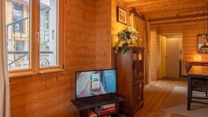 A wooden cabin interior with a television on a stand, a bookshelf, and a dining area. - Maison méserier I T3 I Publier (Publier)