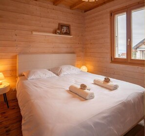 Ein Schlafzimmer einer Holzhütte mit einem Bett, zwei Kissen, einer Nachttischlampe und einem Fenster.