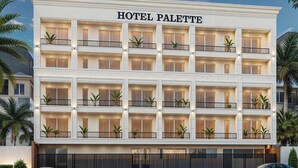 Ett hotell med flera våningar som heter ”HOTEL PALETTE”, med balkonger, en swimmingpool och bilar parkerade framför.