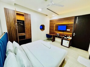 A hotel room with a bed, a desk, a wardrobe, a television, and a ceiling fan. - Palette Hotel & Convention Centre (Gurugram)