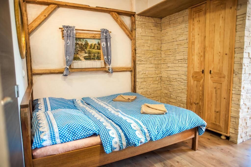 A wooden bed with checkered bedding, a wooden headboard, a small framed picture, and a wardrobe with a stone wall.