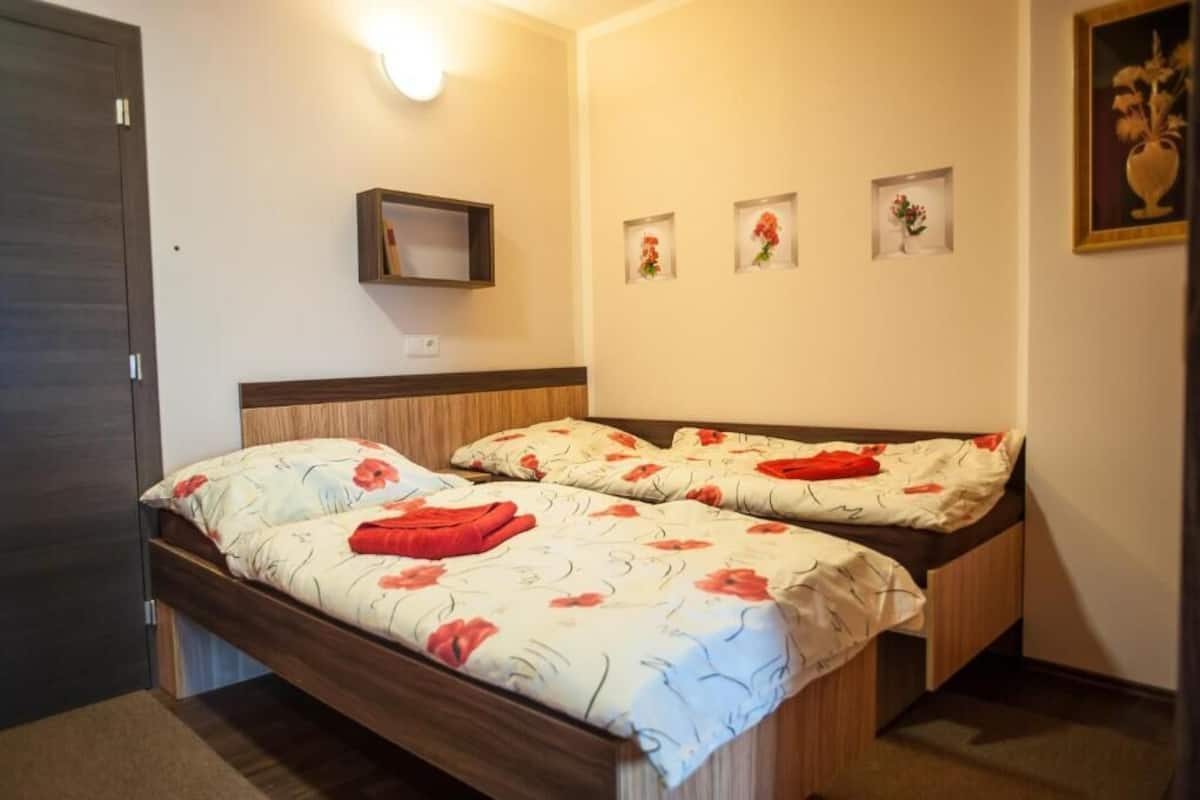 Un lit double avec une literie à motifs floraux, une étagère de chevet et trois tableaux encadrés accrochés au mur.