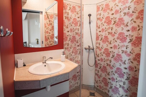 Baño con lavamanos, espejo, ducha y papel tapiz con motivos florales.