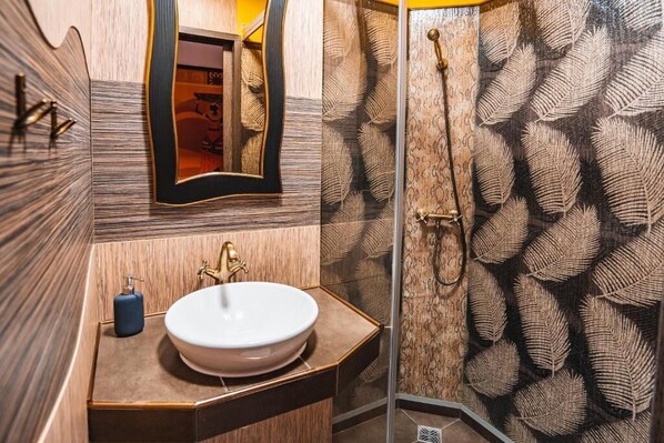 Un baño con un lavabo redondo, un espejo y una ducha con paredes decoradas con motivos de hojas.