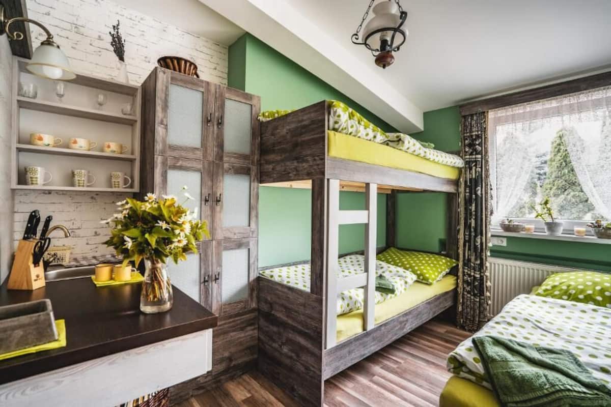 Une chambre avec un lit superposé, une armoire en bois, un vase avec des fleurs et une fenêtre donnant sur des arbres.