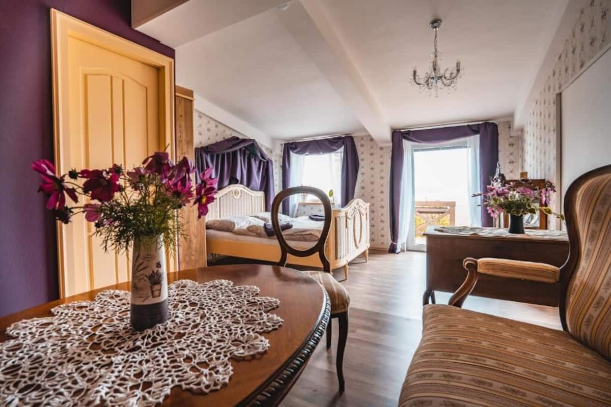 Une pièce avec une table en bois, une chaise, un lit et une fenêtre avec des rideaux.