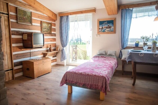 A wooden-paneled room with a bed, a table, a chair, a television, and a window with curtains. - Luční penzion (Česká Skalice)